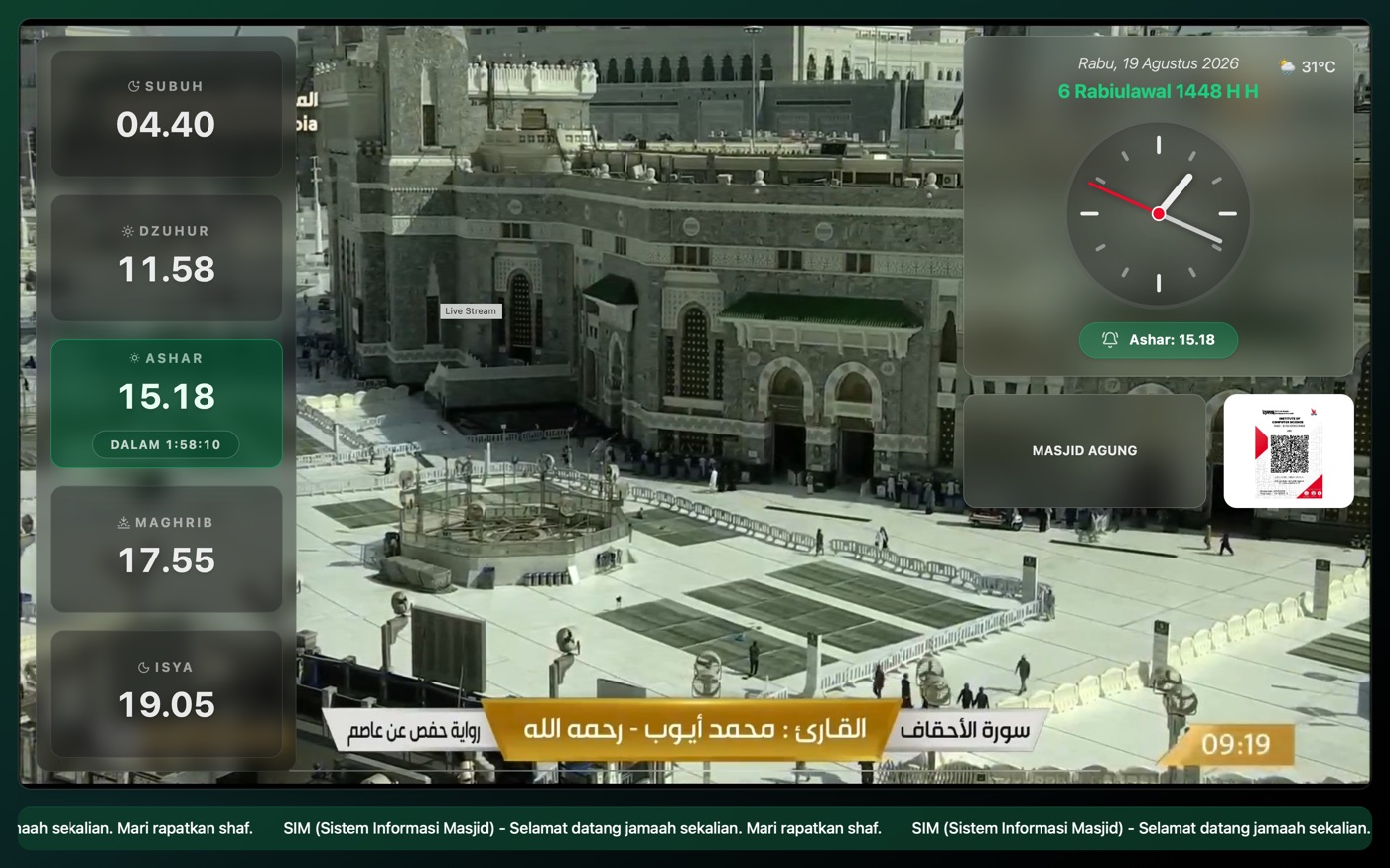 Layar SIM dengan siaran langsung Masjidil Haram sebagai latar penuh, jadwal sholat di kiri, dan jam analog di kanan
